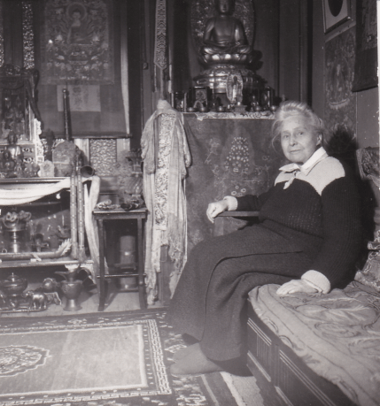 Photographie en noir et blanc de David-Neel assise entourée d'objets tibétains