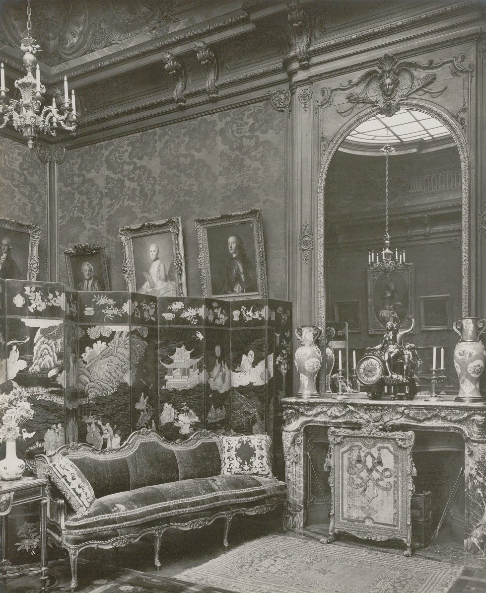 Black and white photograph of a room decorated with paintings and Asian objets