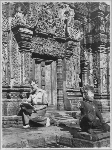 Black and white photograph of Marchal sitting in front of the fake door of a khmer temple 