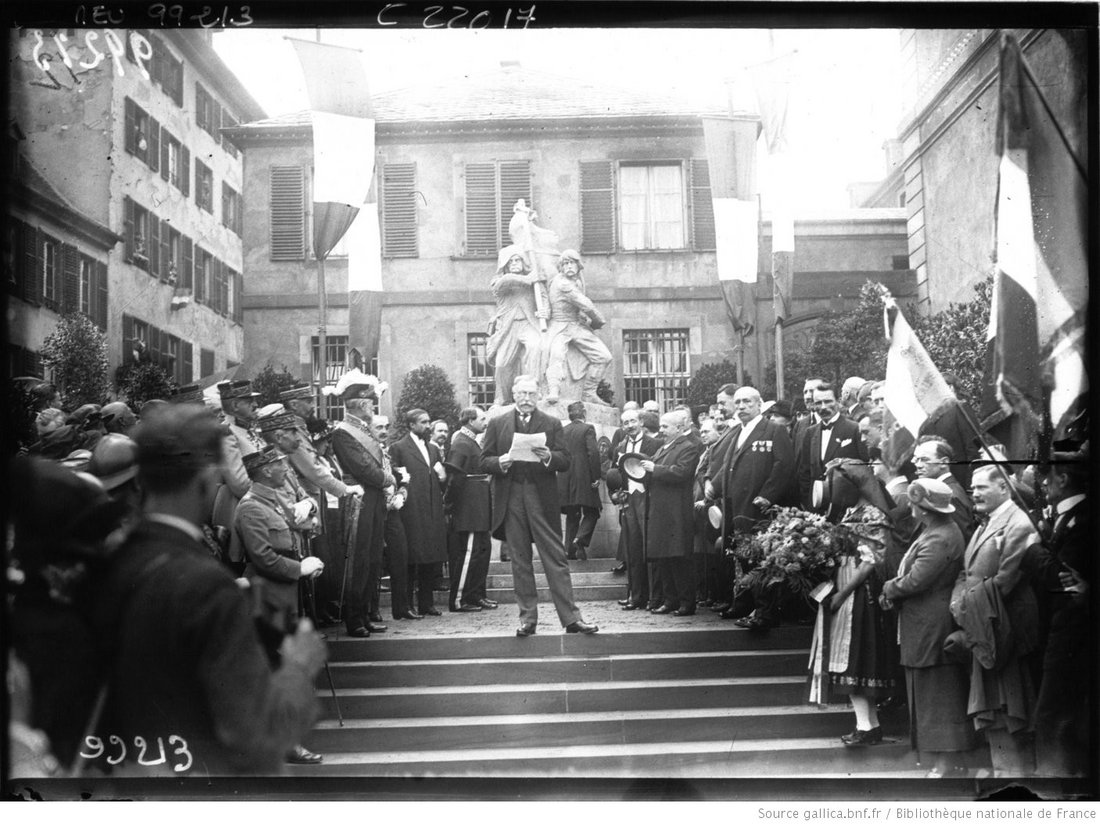 Photographie en noir et blanc d'un groupe de personnes devant un monument, Dietrich est au centre et fait un discours.